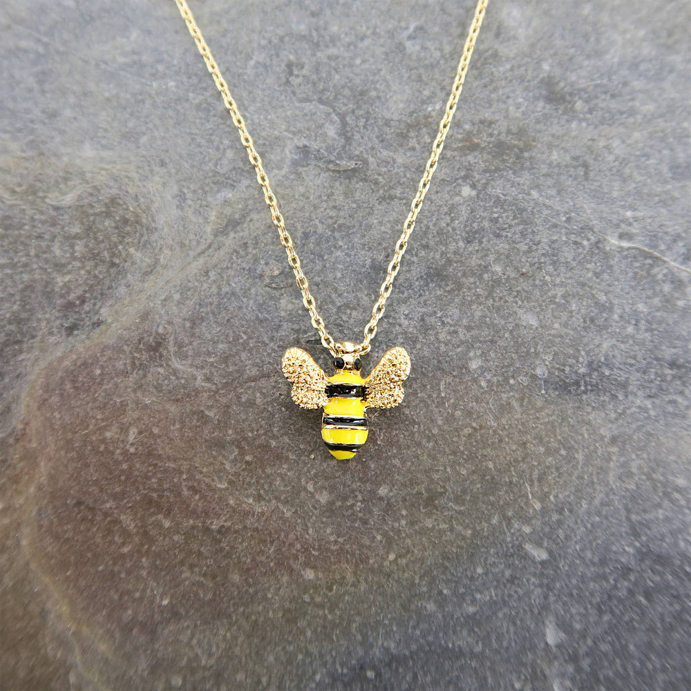 Gold bee-shaped pendant necklace on a stone surface