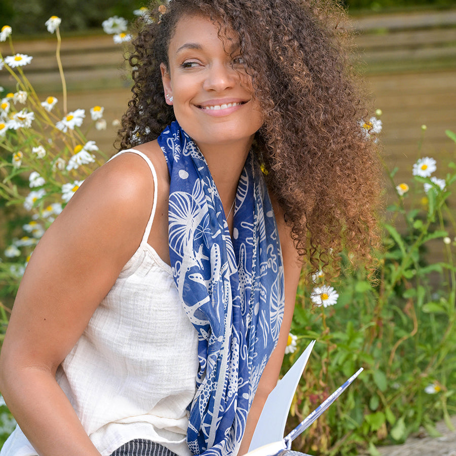 Woman wearing a blue patterned scarf outdoors with flowers in the background