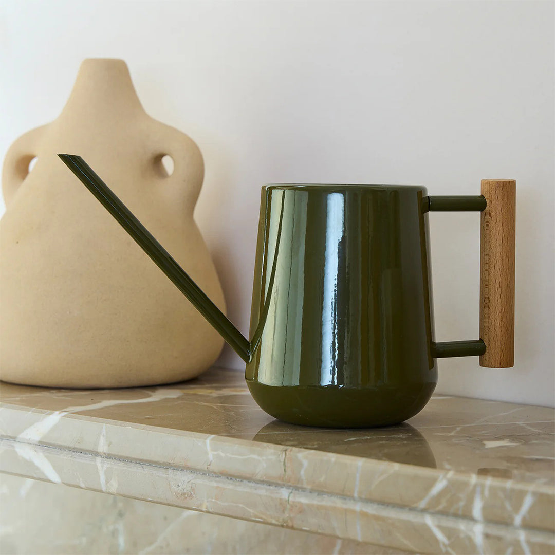 Green watering can with wooden handle on a marble surface