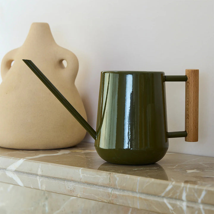 Green watering can with wooden handle on a marble surface