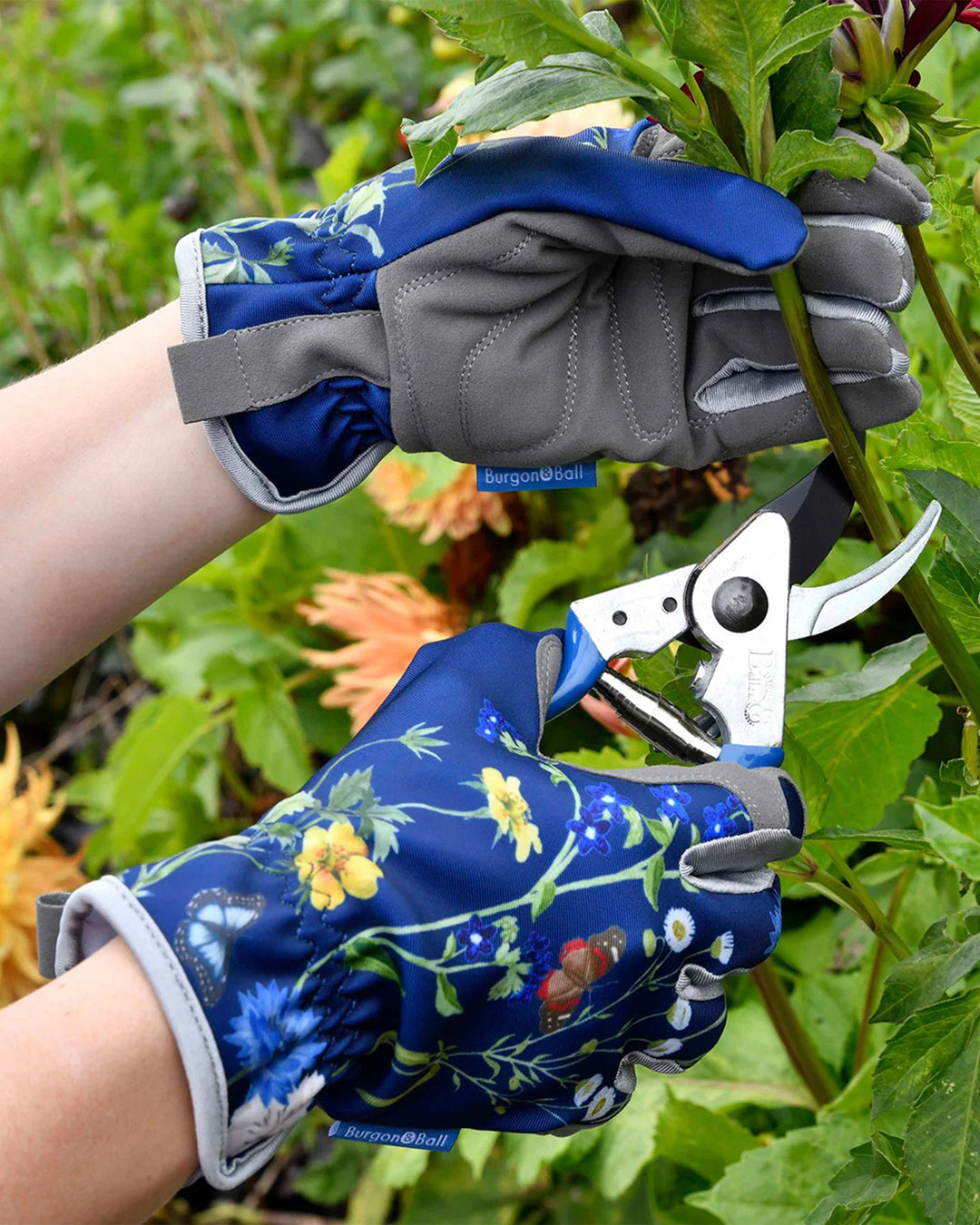 Person wearing floral gardening gloves holding garden shears in a garden setting