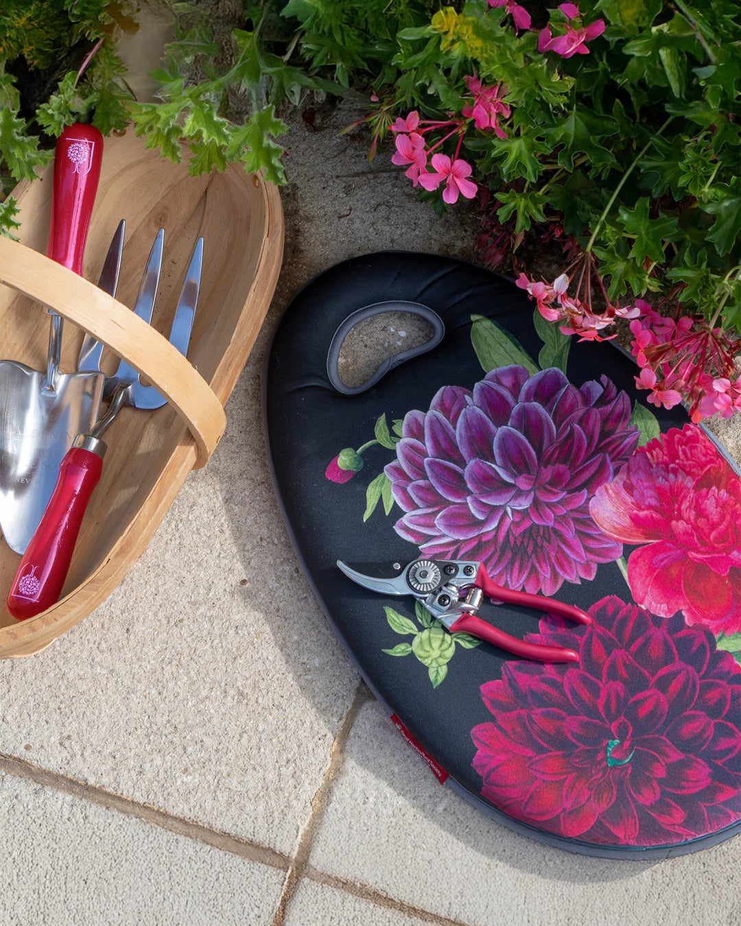 Gardening tools including a trowel and pruner on a floral-patterned tray with pink flowers in the background.