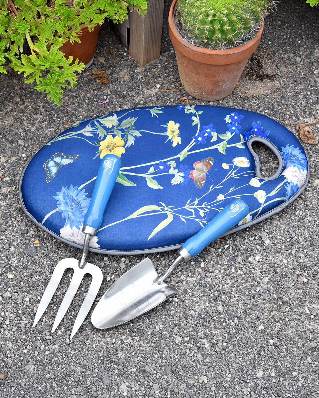Gardening tools with a floral-patterned blue mat on a concrete surface.
