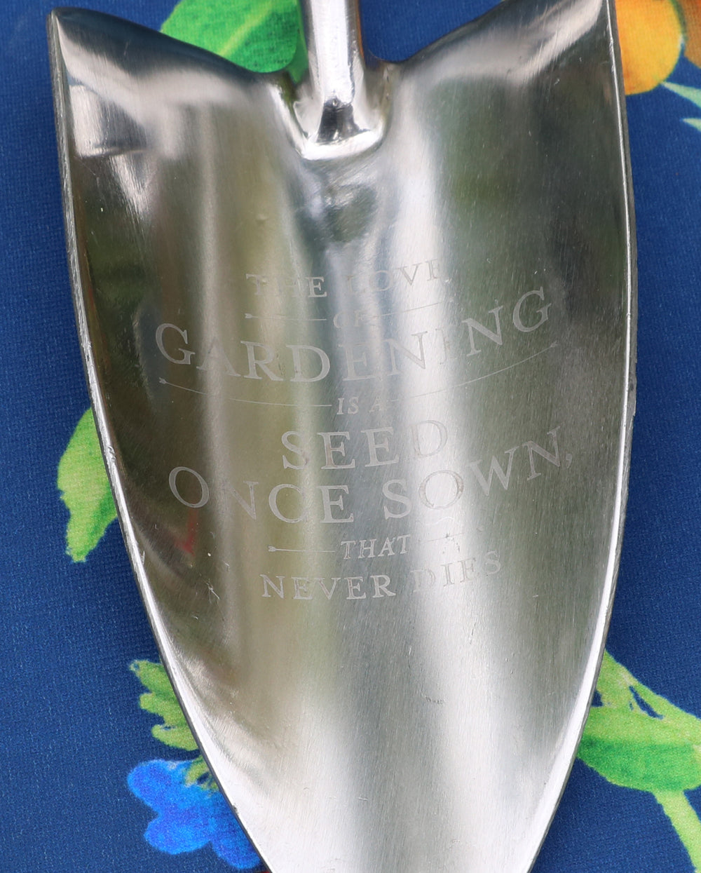 Metal gardening trowel with engraved text on a blue floral background