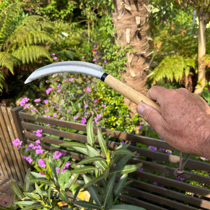 Hand holding a gardening tool with a blurred garden background