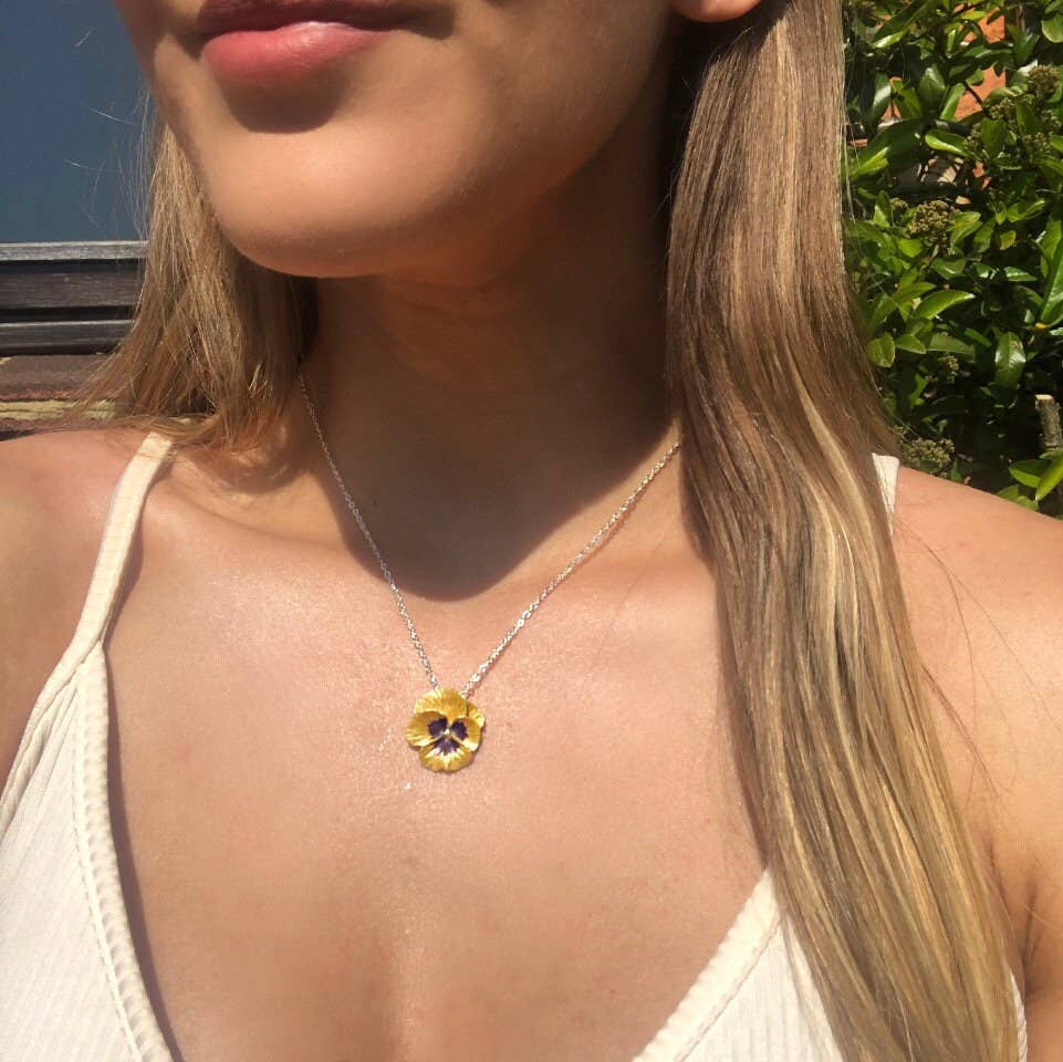 Close-up of a woman wearing a necklace with a floral pendant outdoors.