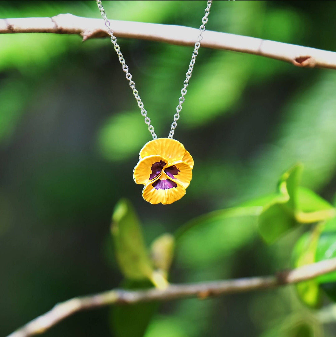 Yellow flower pendant necklace on a branch with green leaves