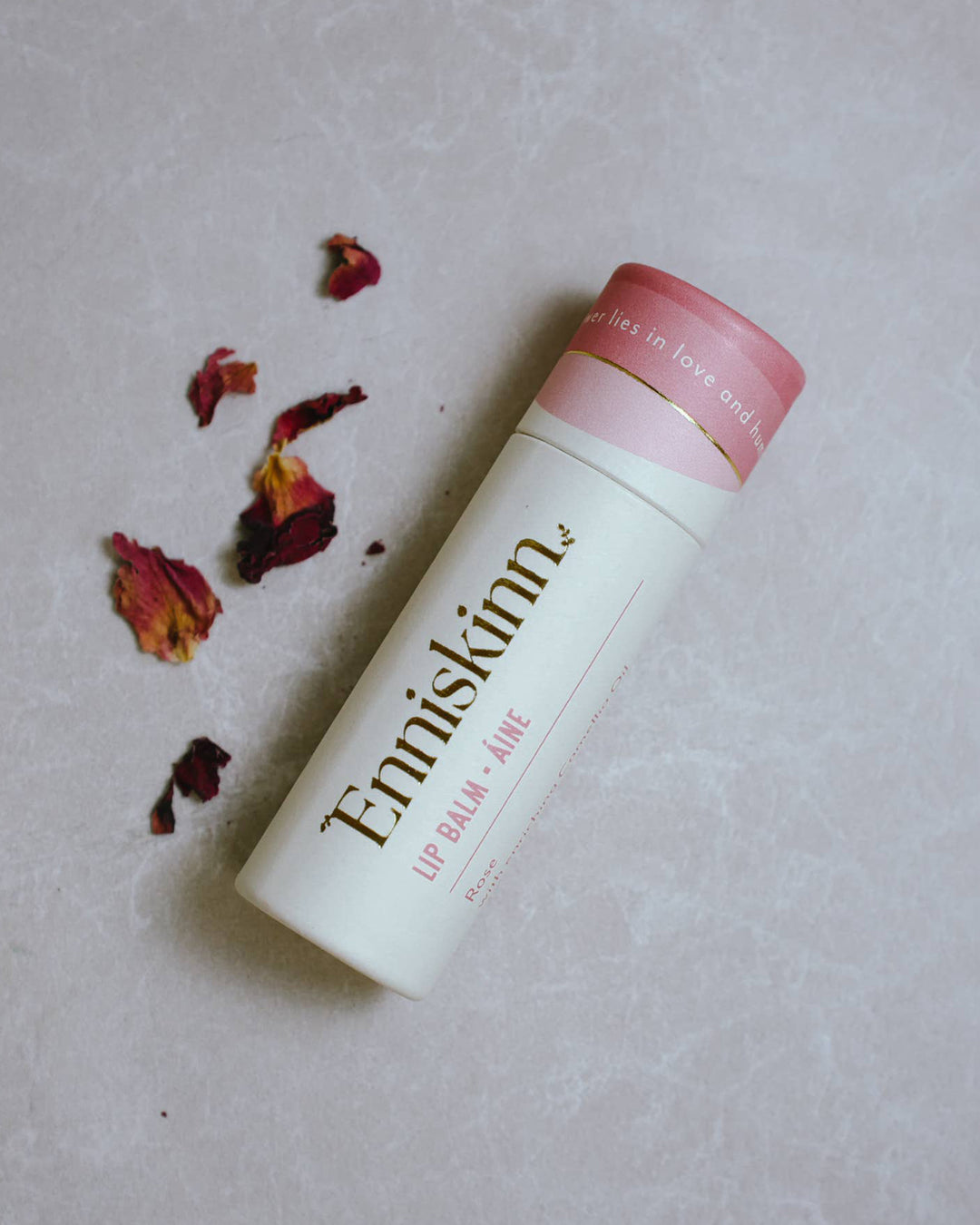 Lip balm tube with pink cap and visible brand name on a light background with dried flowers.