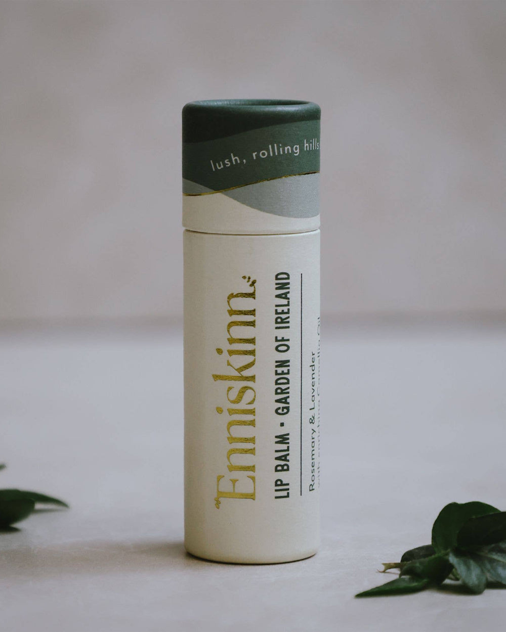 Enniskinn lip balm container on a light background with green leaves.