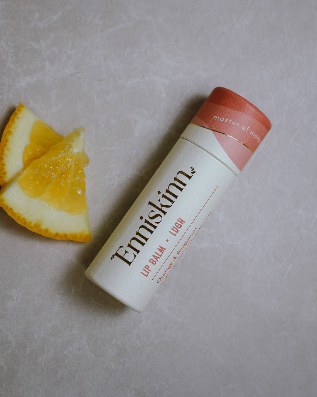 Enniskinn lip balm with orange slices on a gray surface