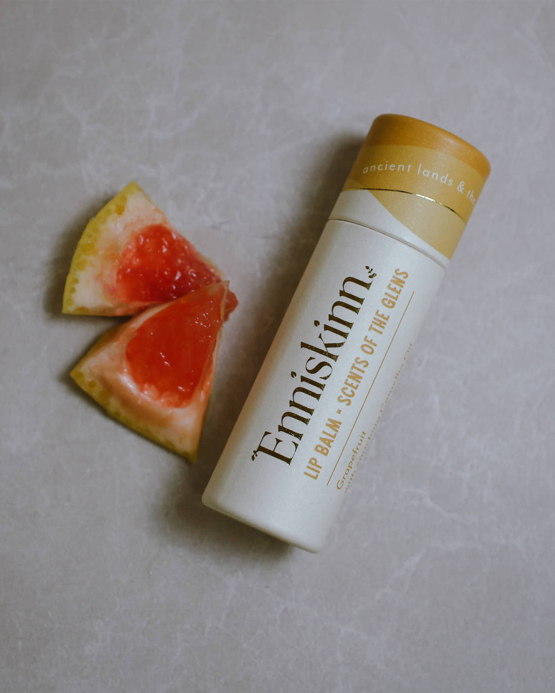 Enniskinn lip balm with a slice of grapefruit on a gray surface