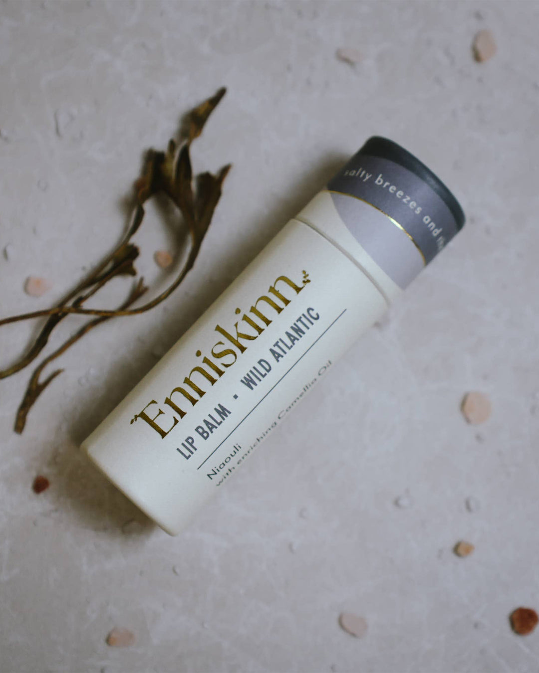 Enniskinn lip balm on a textured surface with dried plants