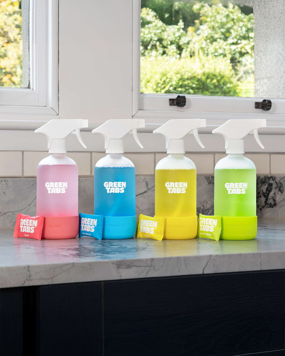 Four spray bottles with colorful bases and 'Green Tabs' branding on a kitchen counter.