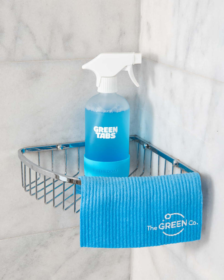 Cleaning products including a spray bottle and microfiber cloth on a shower caddy with 'The GREEN Co.' branding.