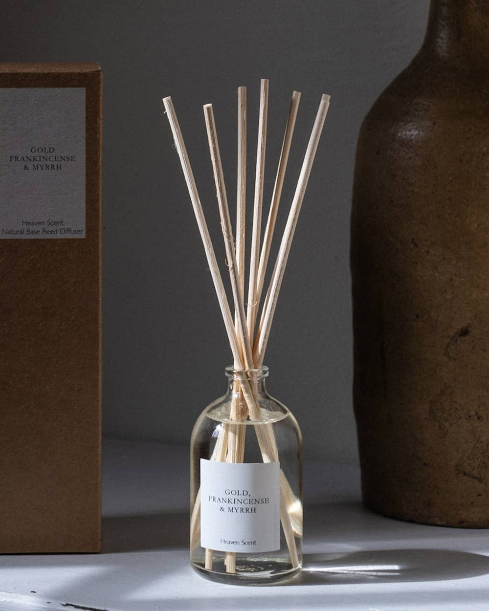 Glass diffuser bottle with wooden sticks on a grey surface with a dark background