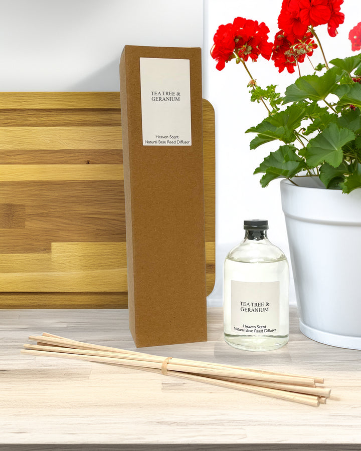 A glass bottle and reeds as part of a reed diffuser kit with box on a counter top with red flowered geranium