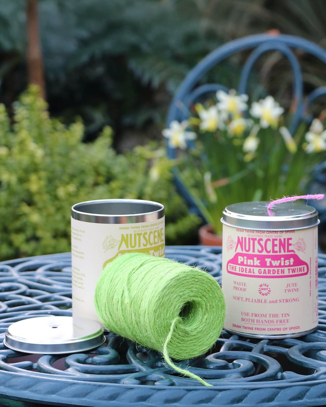 Two cans of Nutscene with a green yarn roll on a garden table.