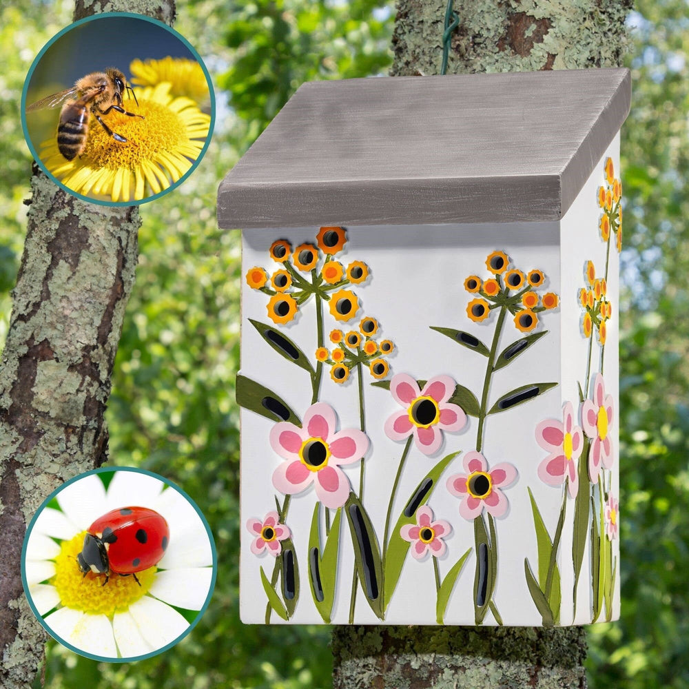 Decorative bee house with floral design on a tree trunk, surrounded by nature.