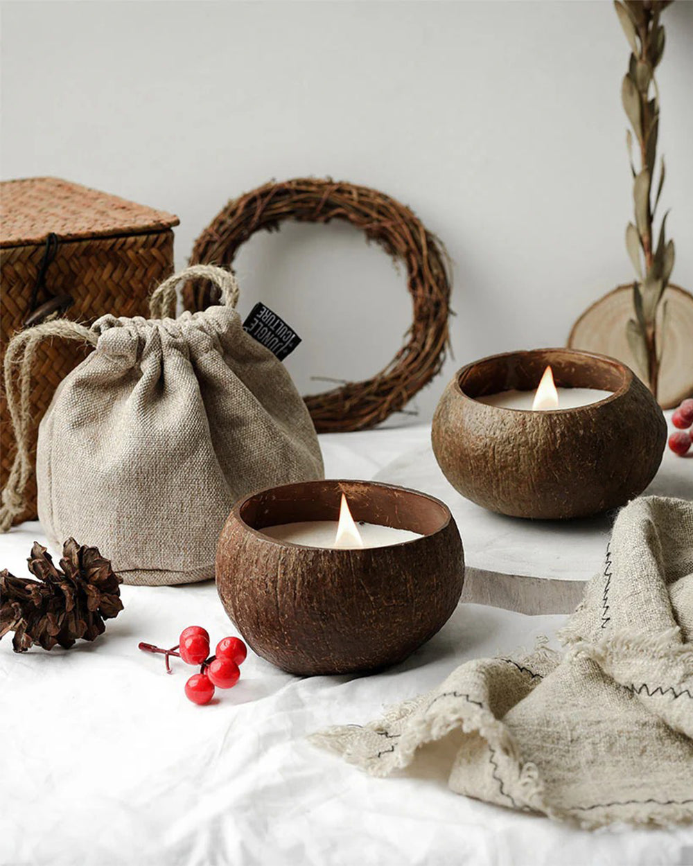 Coconut shell candles on a white surface with a woven bag and decorative elements.