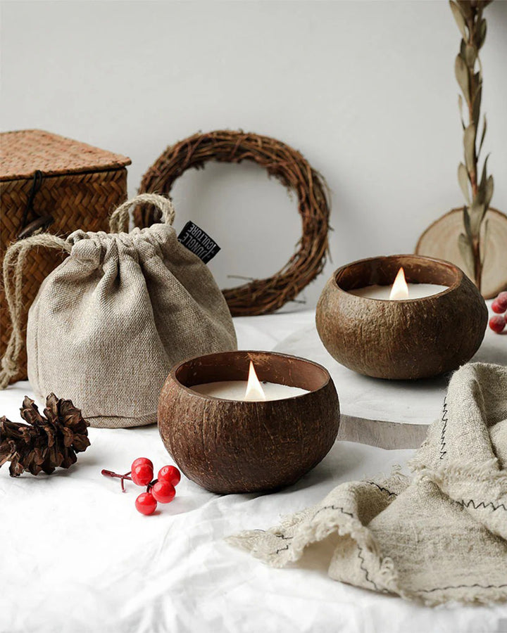 Coconut shell candles on a white surface with a woven bag and decorative elements.