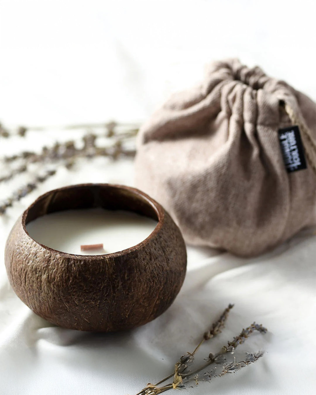 Candle in a coconut shell with a drawstring bag and lavender on a white background