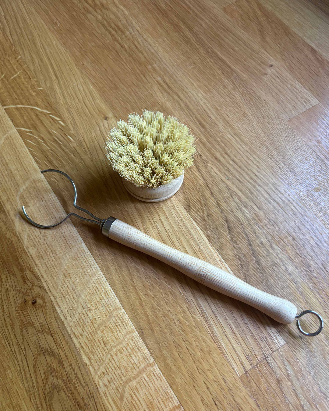 Dish brush with wooden handle and metal hook on a wooden floor