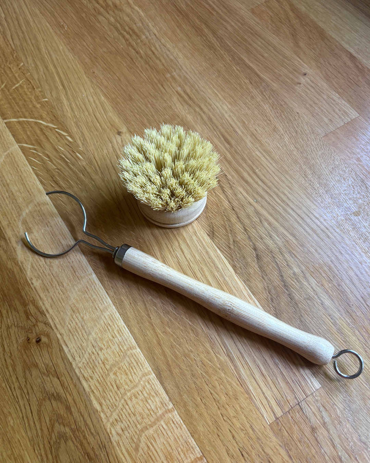 Dish brush with wooden handle and metal hook on a wooden floor