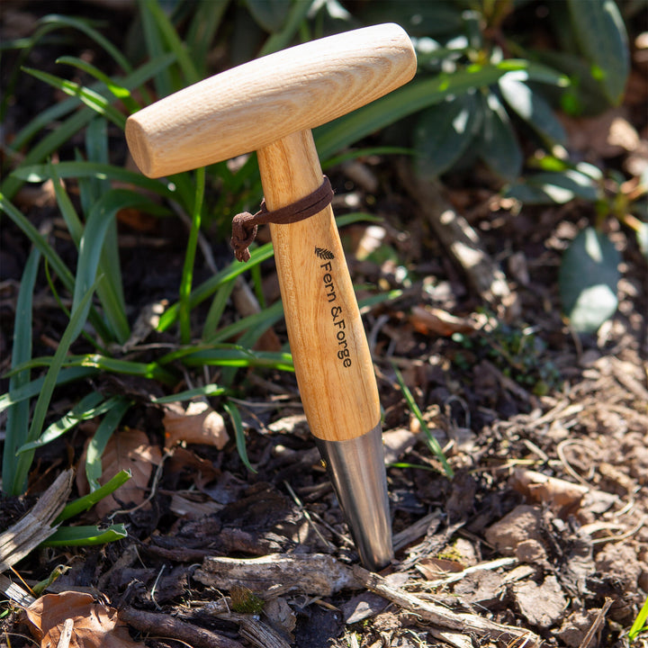 Close view of the Nutscene Fern and Forge hand dibber showing the branded ash T handle and tapered point against spring foliage