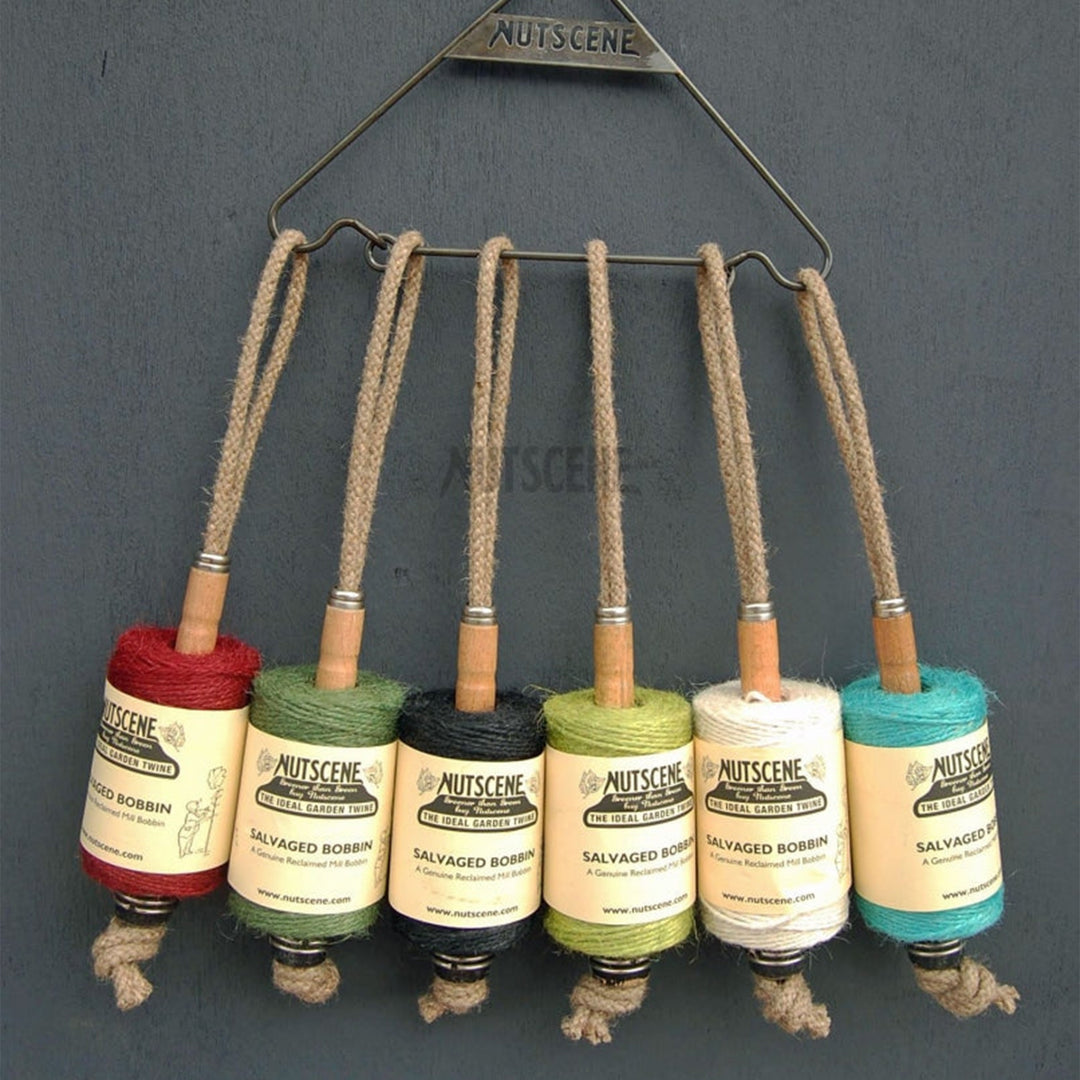 Six Nutscene jute twine spools on reclaimed Lancashire mill bobbins hanging from a wire hanger, including the green colourway