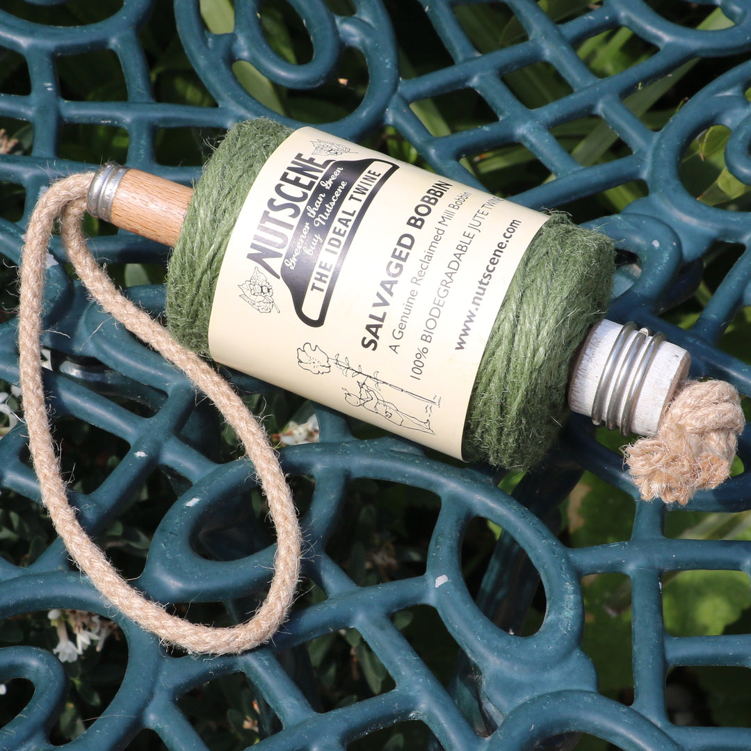 A spool of green jute twine on a salvaged mill bobbin on a dark green ornate metal garden table outdoors.