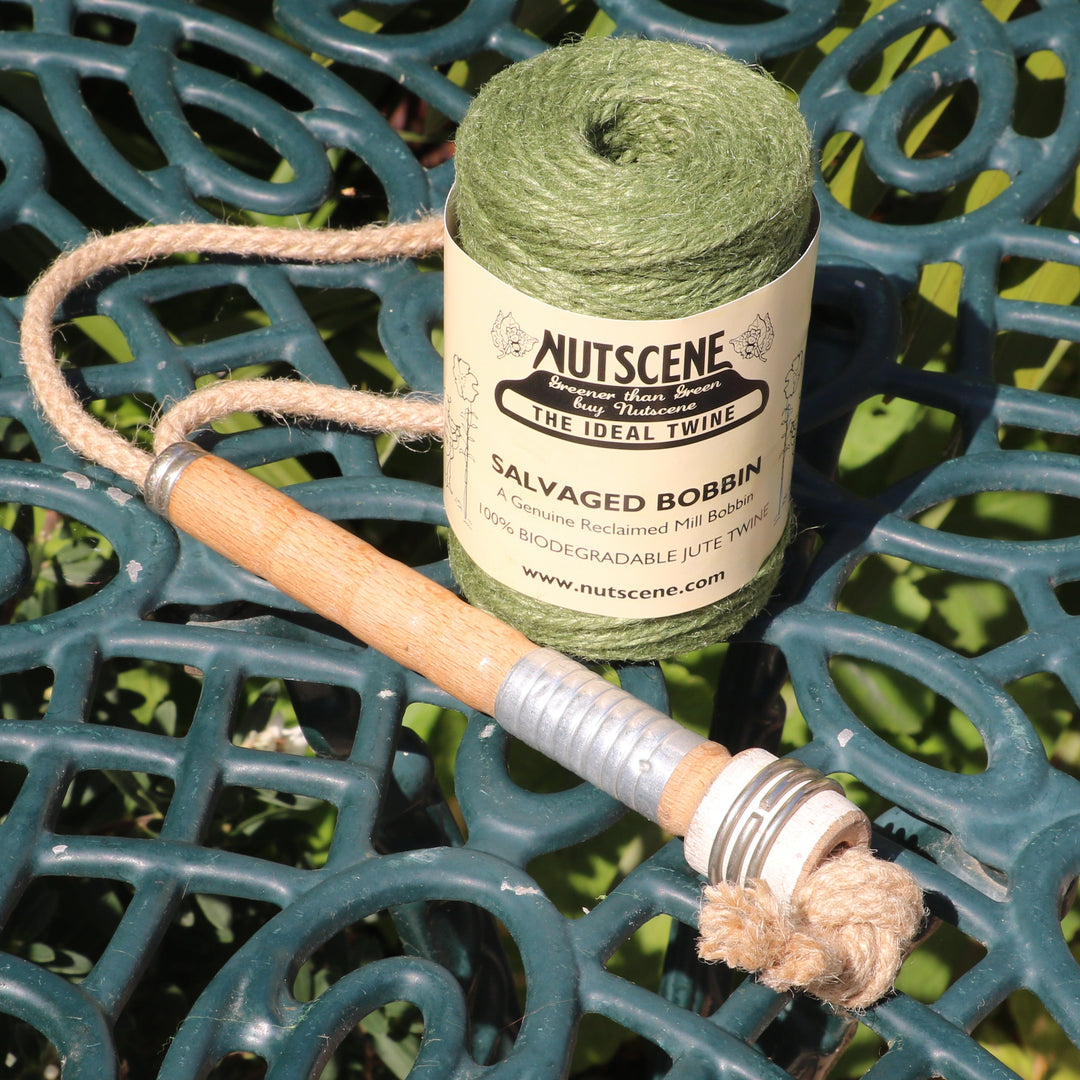 A spool of green jute twine on a salvaged mill bobbin on a dark green ornate metal garden table outdoors.