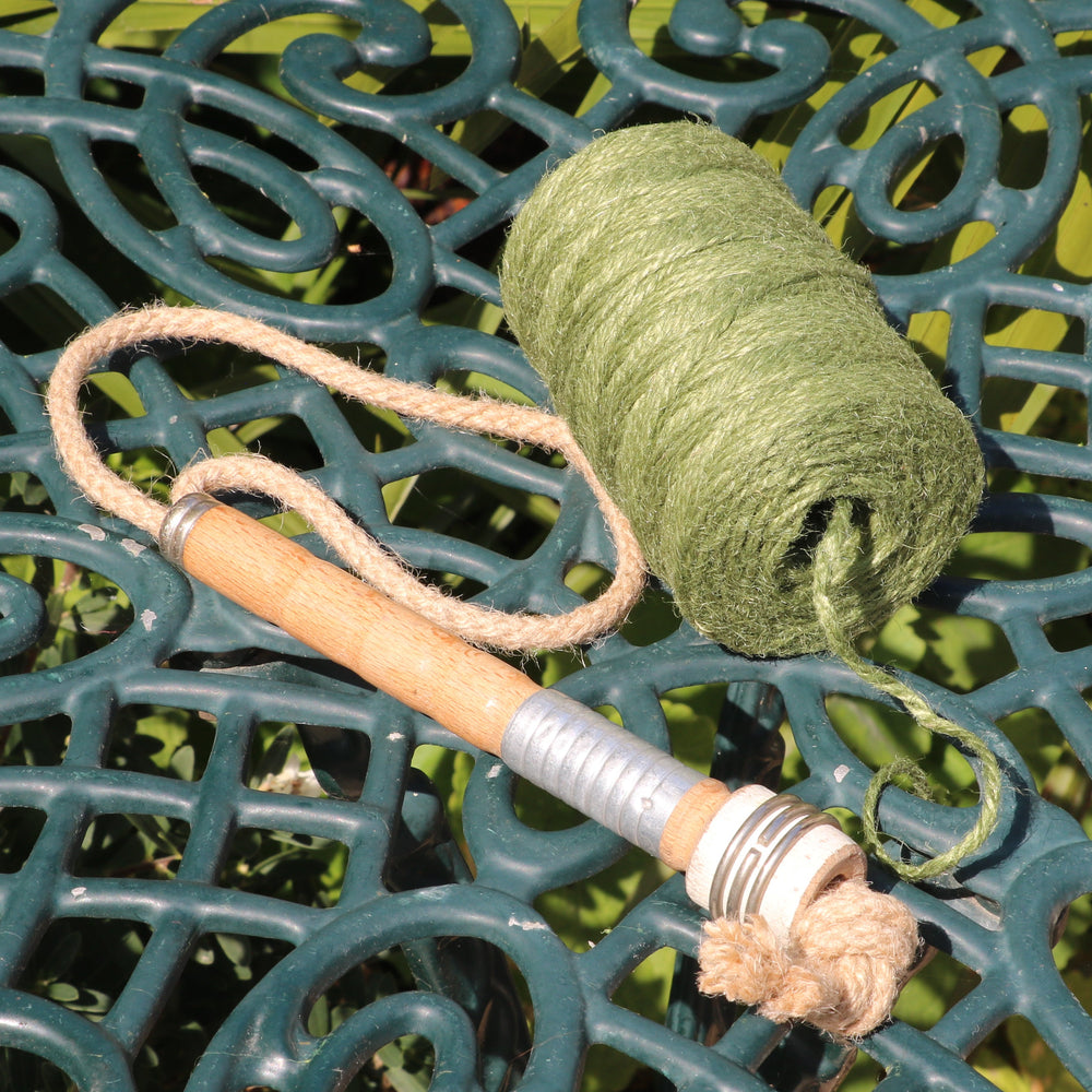 A spool of green jute twine with a salvaged mill bobbin on a dark green ornate metal garden table outdoors.