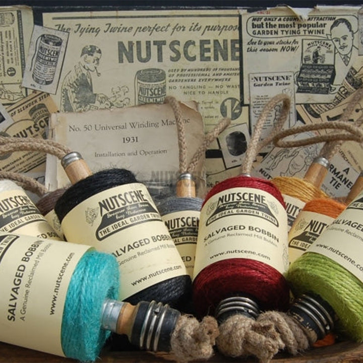 Nutscene jute twine spools on reclaimed Lancashire mill bobbins including the red colourway, arranged on vintage Nutscene print
