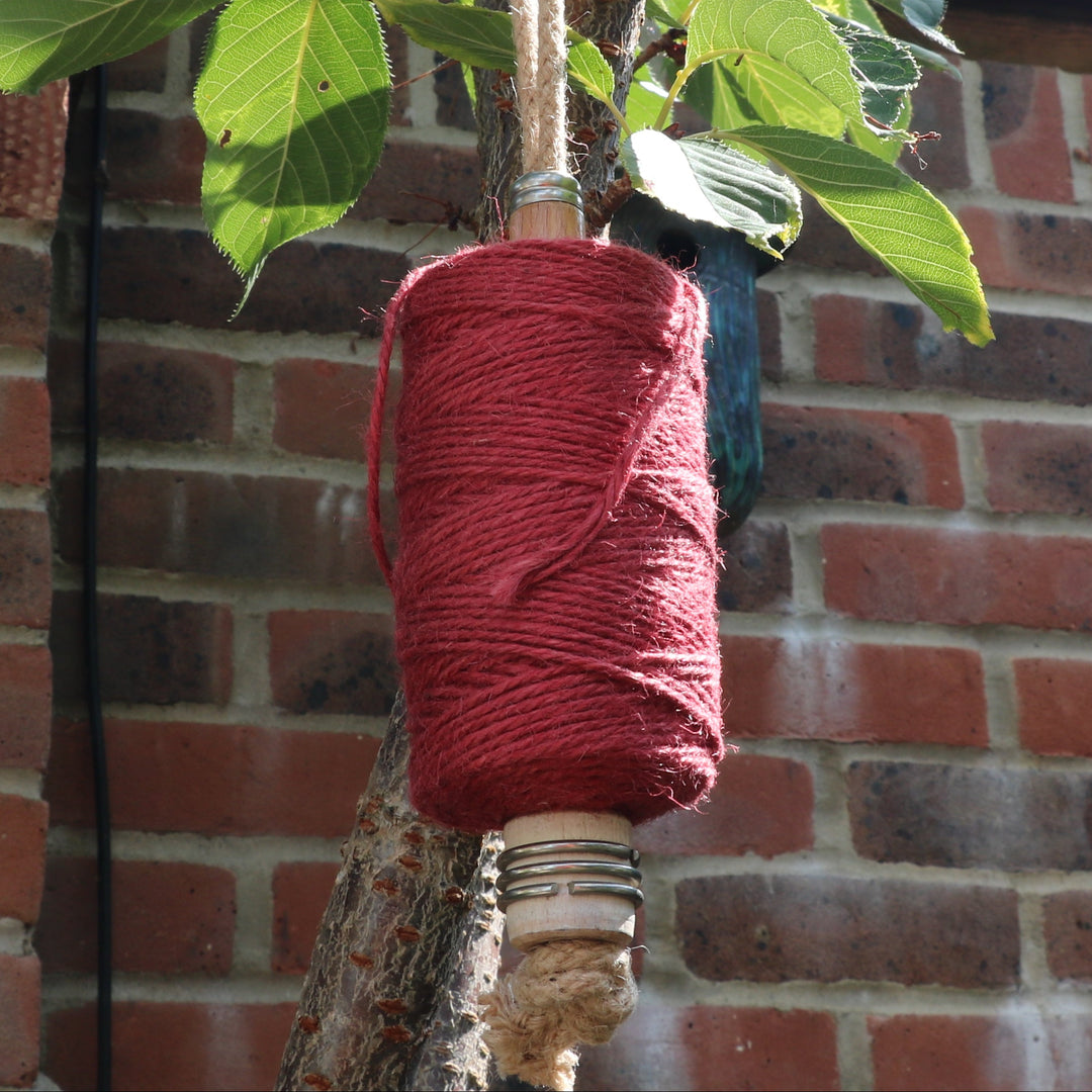 Spool of garden twine on a mill bobbin loop hanging from a tree and a brick wall background.