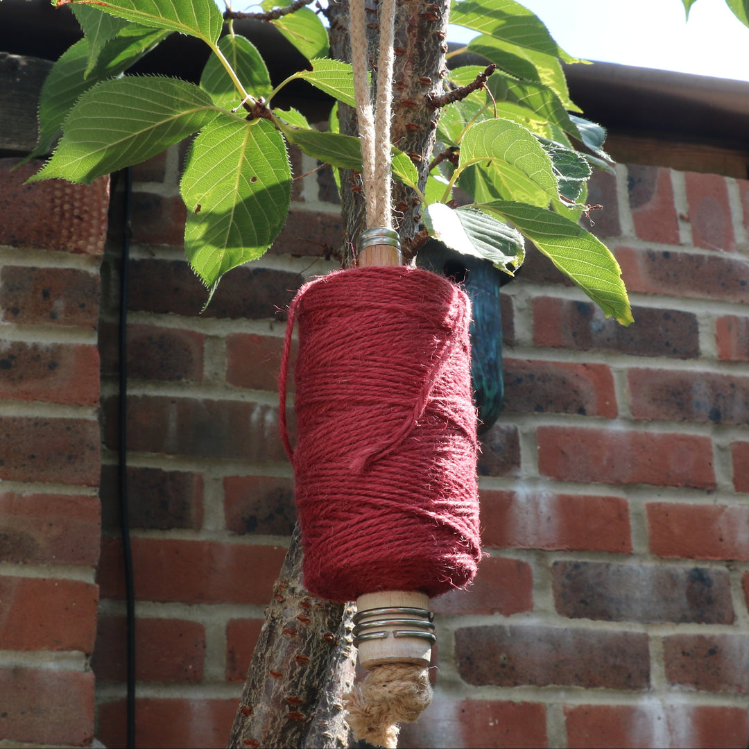 Spool of garden twine on a mill bobbin loop hanging from a tree and a brick wall background.