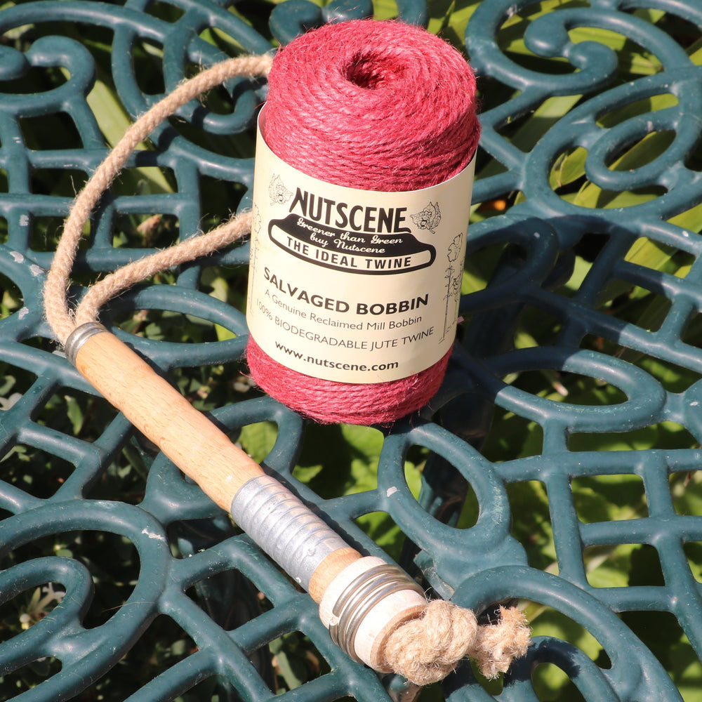 A spool of Nutscene Salvaged Bobbin garden twine in red sits on a dark green ornate metal patio table.