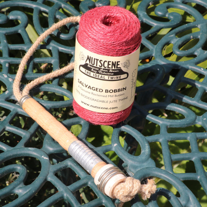 A spool of Nutscene Salvaged Bobbin garden twine in red sits on a dark green ornate metal patio table.