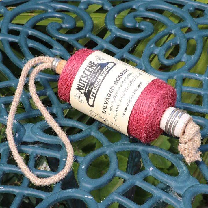 A spool of Nutscene Salvaged Bobbin garden twine in red sits on a dark green ornate metal patio table.