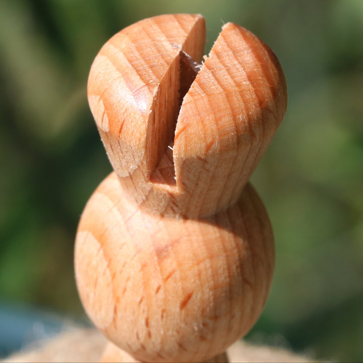 A close-up of a twine cutting notch in a wooden twine stand, photographed outdoors against a blurred green natural background.