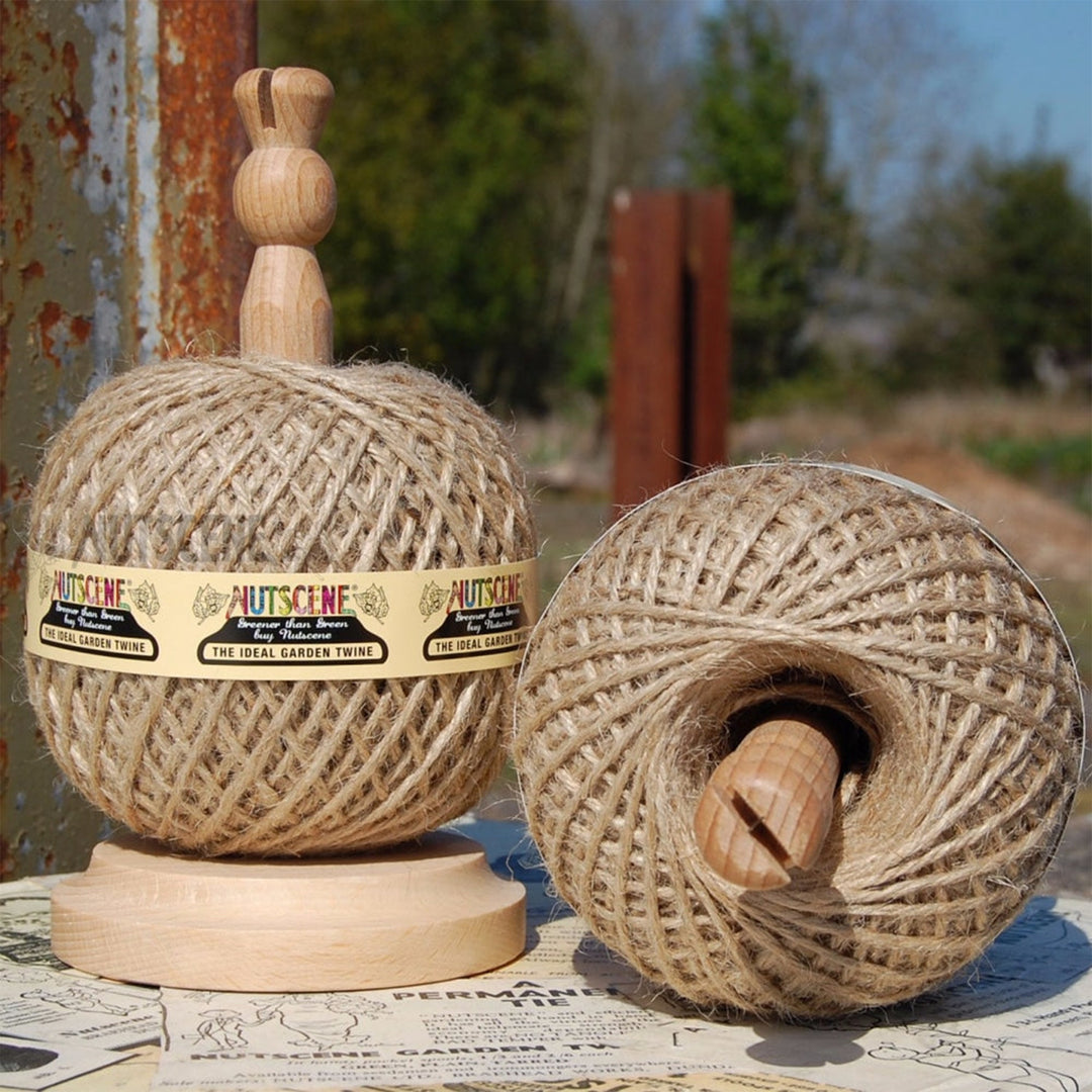 Nutscene wooden twine holder with a ball of natural jute twine in place, photographed outdoors beside a second ball showing the beech base