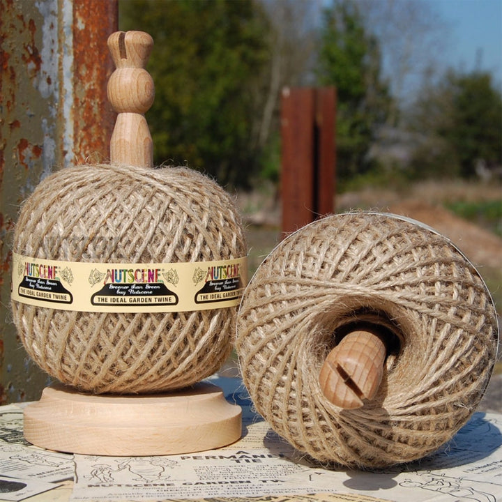 Nutscene wooden twine holder with a ball of natural jute twine in place, photographed outdoors beside a second ball showing the beech base