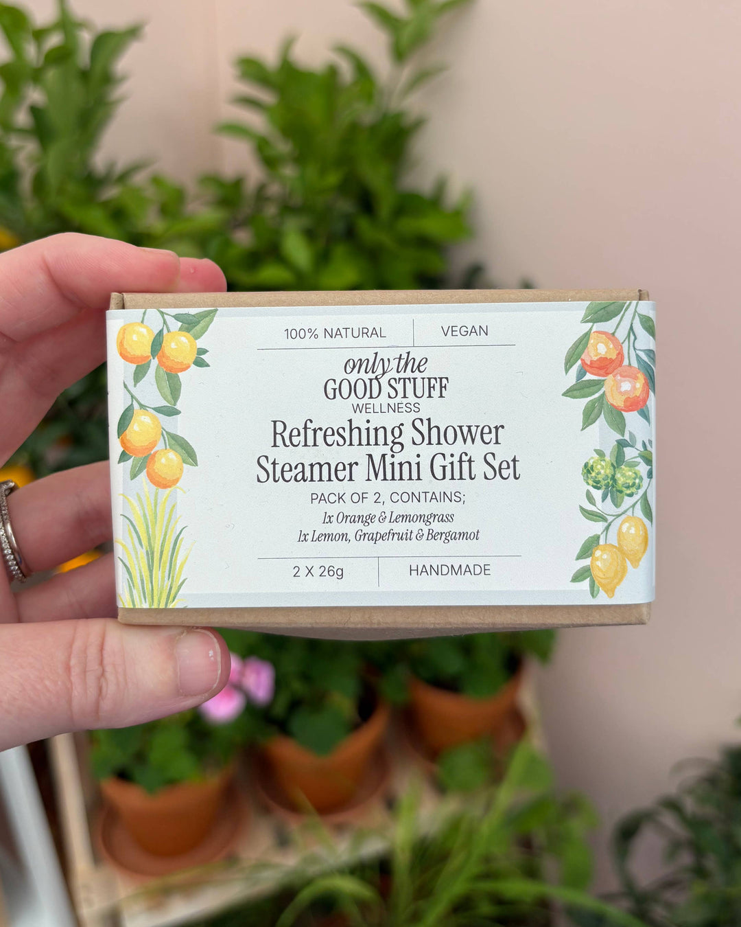 Hand holding a 'only the good stuff' shower steamer mini gift set with plants in the background