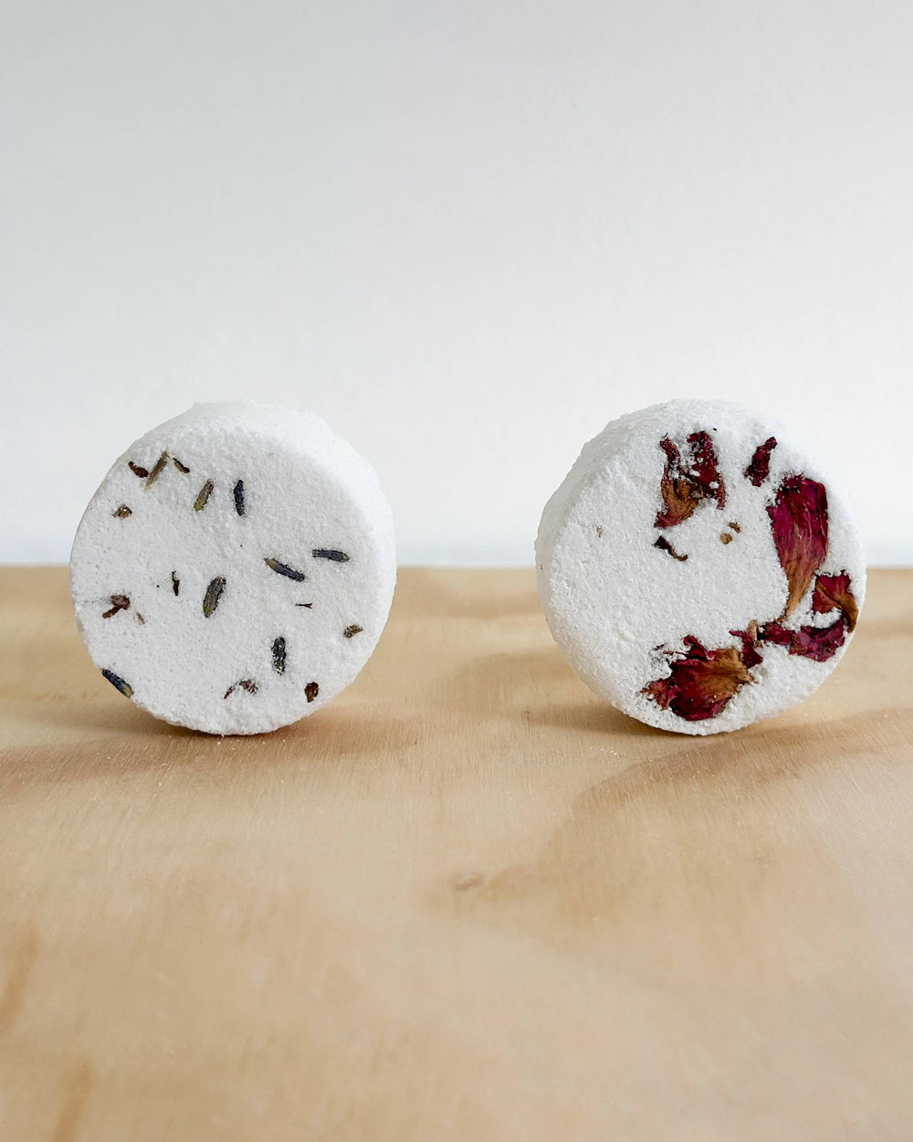 Two round bath bombs with natural ingredients on a wooden surface