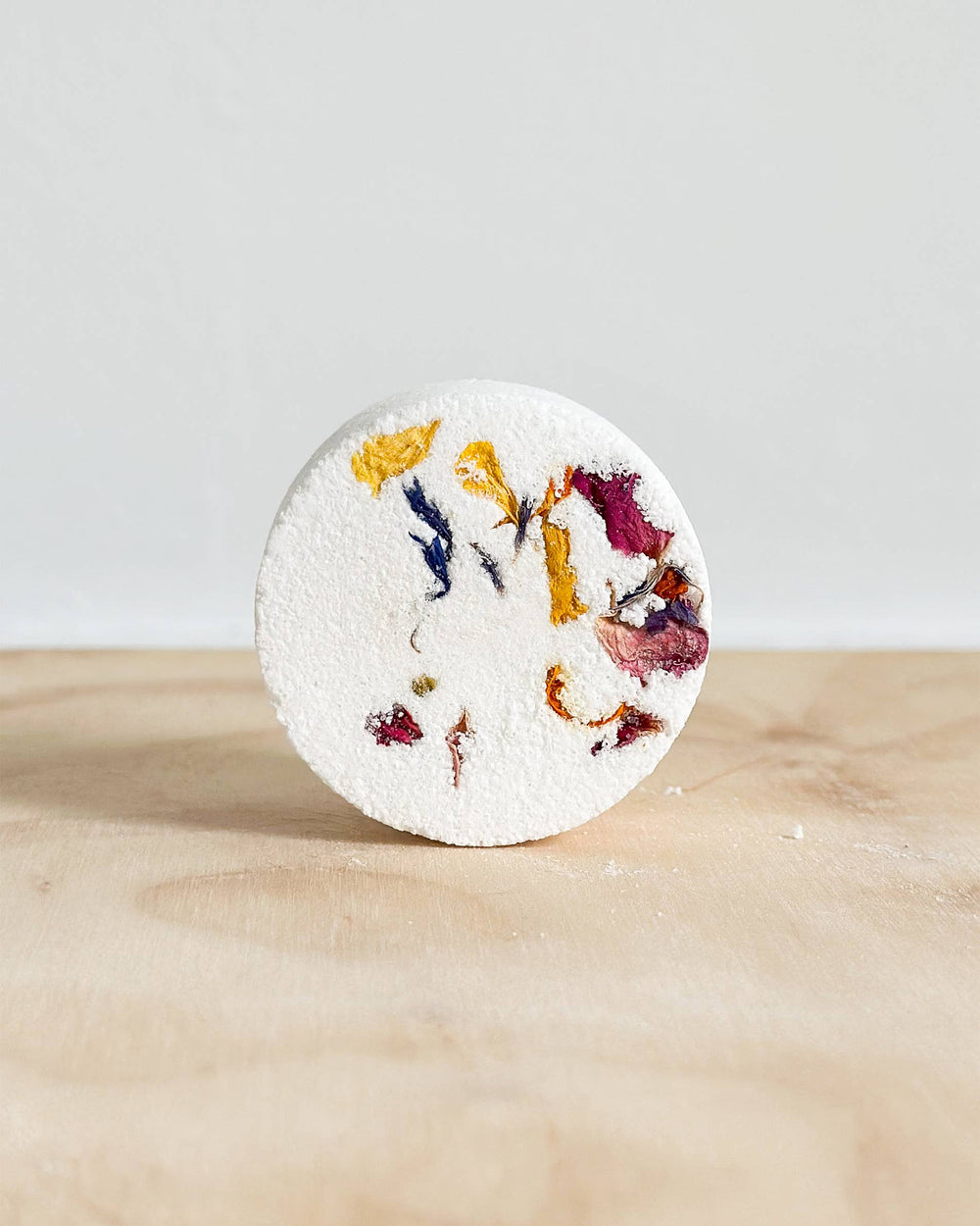 Round shower steamer with colourful floral petals on a wooden surface