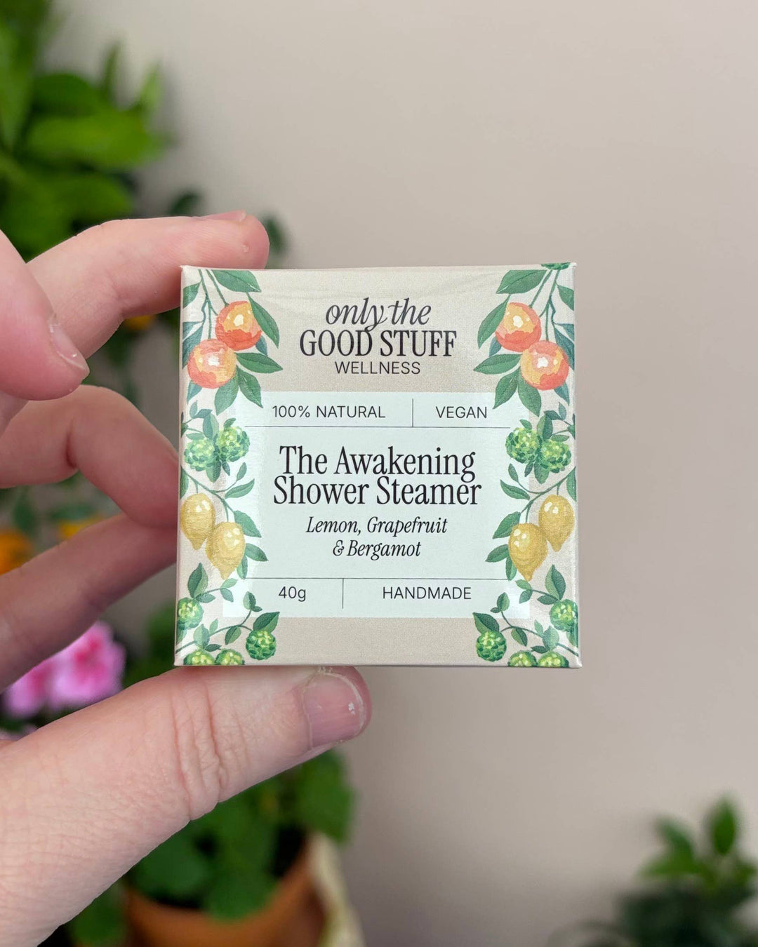 Hand holding a 'only the GOOD STUFF' shower steamer packaging with plants in the background