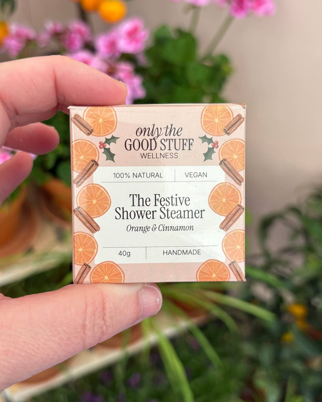 Hand holding a box of 'only the Good Stuff Wellness' shower steamer with orange and cinnamon design.
