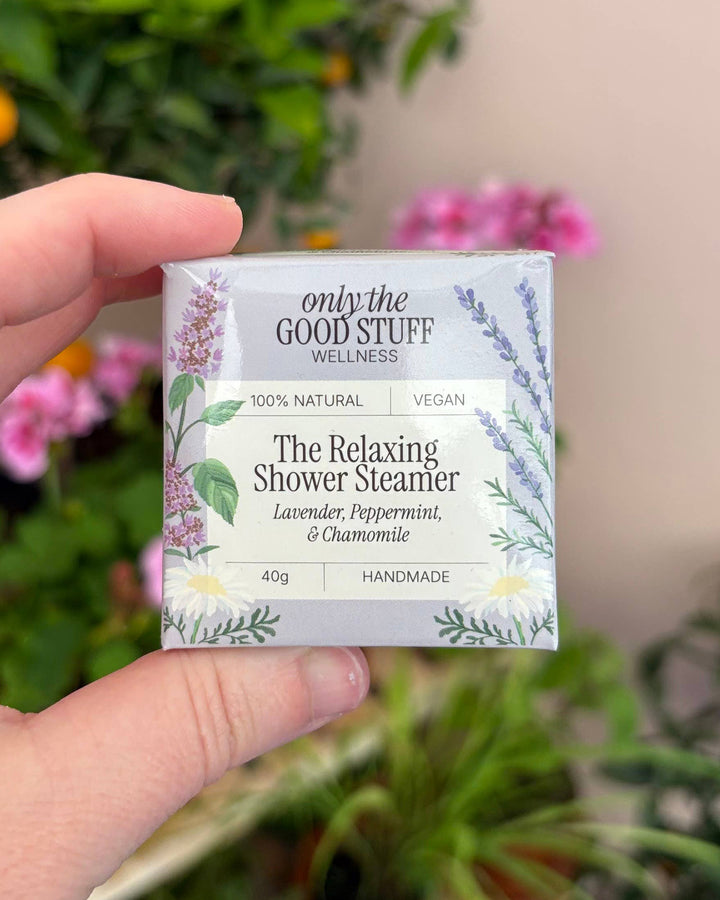 Hand holding a box of 'only the Good Stuff' Relaxing Shower Steamers with a garden background.