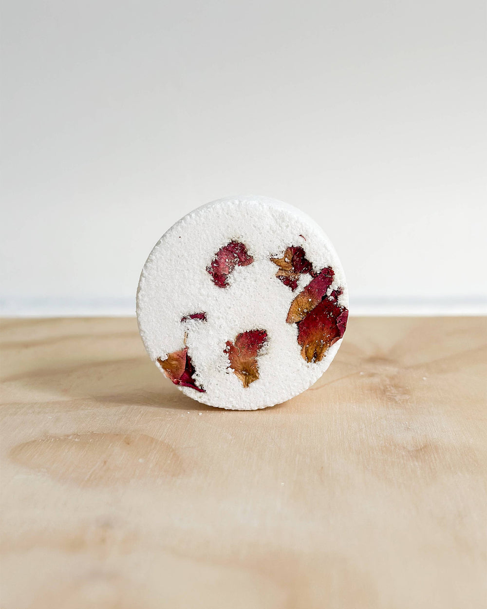 Round shower steamer with dried flowers on a wooden surface