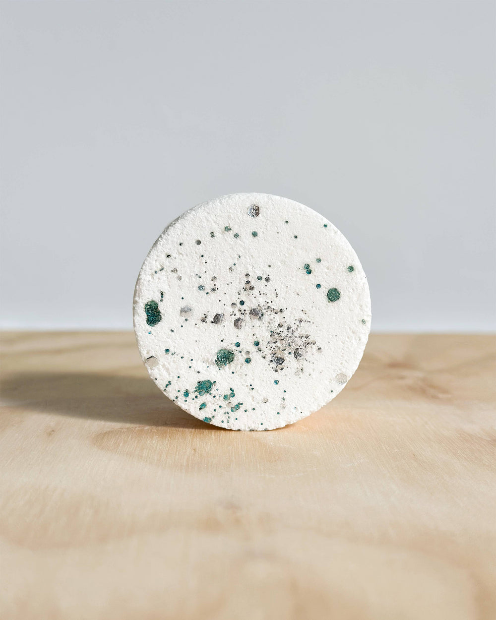 Round concrete coaster with speckled pattern on a wooden surface