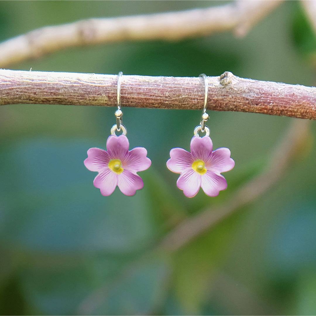 Pink flower-shaped earrings hanging on a branch with a blurred green background
